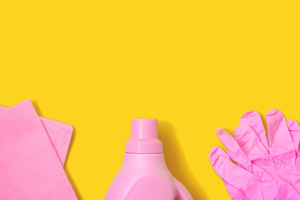 Różowa szmata, plastikowa butelka i gumowe rękawiczki na żółtym tle. Koncepcja czyszczenia - Zdjęcie, obraz