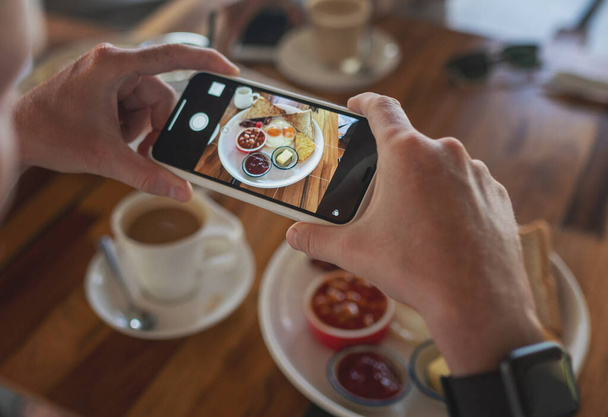 Photo of food on a smartphone in a cafe, male hands take a picture of a breakfast of scrambled eggs. - Foto, immagini