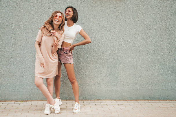 Two young beautiful smiling hipster girls in trendy summer clothes.Sexy carefree women posing on street background in sunglasses. Positive models having fun and hugging - Foto, afbeelding