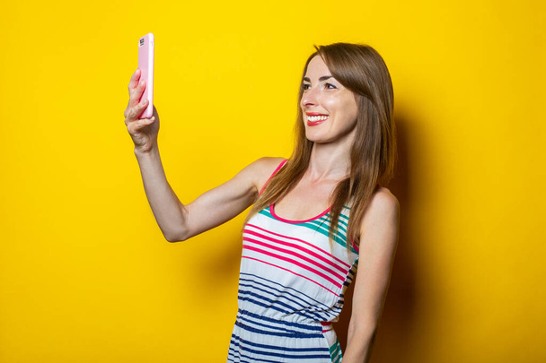 Young woman holding a phone communicates by video chat on a yellow background - Фото, зображення