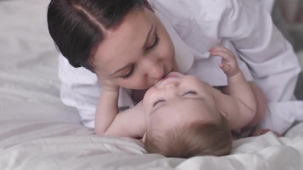 Gelukkige moeder die haar zoontje kust en lacht. rusten in bed samen gelukkig gezin moederschap  - Video