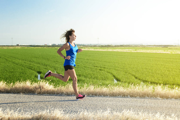Egy fiatal atléta lány kék ingben fut végig a rizsföldek közti úton, tükörképével a rizsvízben. - Fotó, kép