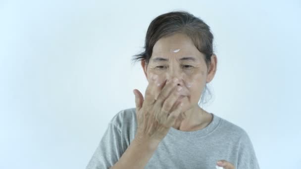 Beauty concept. An old woman applying cream on a white background. 4k Resolution. - Video