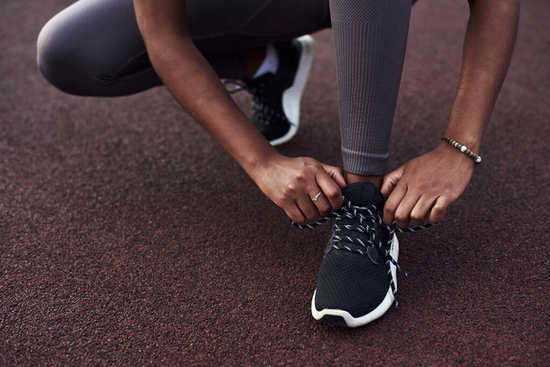 Chica negra ata sus zapatillas de deporte mientras hace deportes en la calle. Concepto de fitness al aire libre. - Foto, Imagen