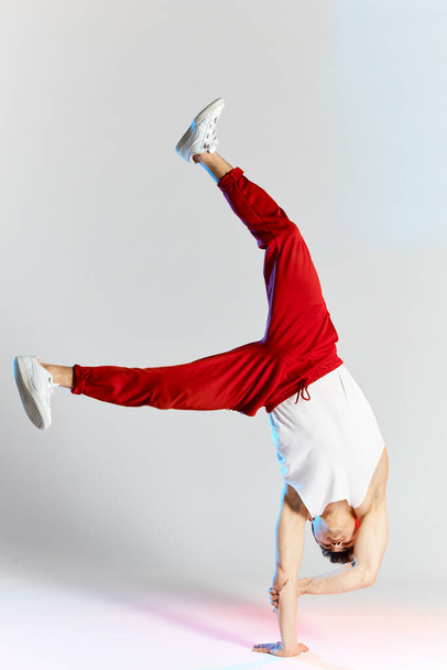 Young man in red sweatpants doing a handstand on hands on white background - Valokuva, kuva