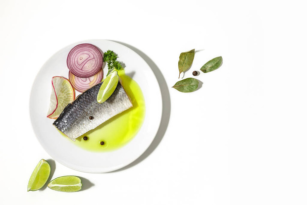 Salted herring with spices, lime slices and red onion rings on a white background. copy space. Flat lay. - Photo, Image