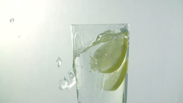 Pieces of lemon fall into glass of water whilst water spills over the edge - Πλάνα, βίντεο