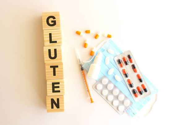 Слова GLUTEN зроблені з дерев'яних кубиків на білому тлі з медичними препаратами та медичною маскою. Медична концепція
. - Фото, зображення