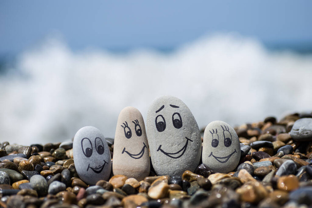 Group of stones with drawn faces in the sand. Father, mother, daughter and son. Concept of happy family. - Photo, Image