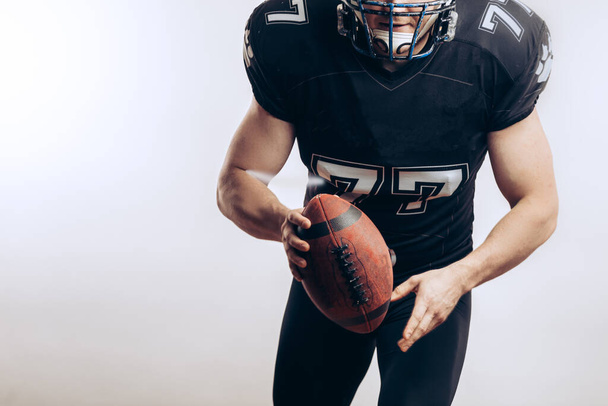 Muscular american football player in protective uniform and helmet holding ball - Φωτογραφία, εικόνα