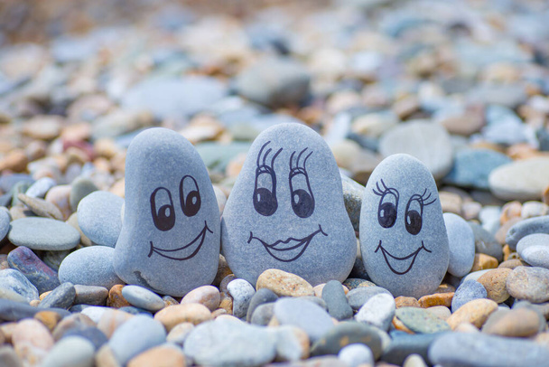 Камушек с нарисованными лицами в песке. Отец, мать и дочь. Концепция семейного отдыха - Фото, изображение