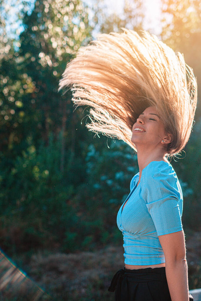 Νεαρή γυναίκα κοντά σε ένα δάσος που πετάει τα μαλλιά της στον αέρα - Φωτογραφία, εικόνα