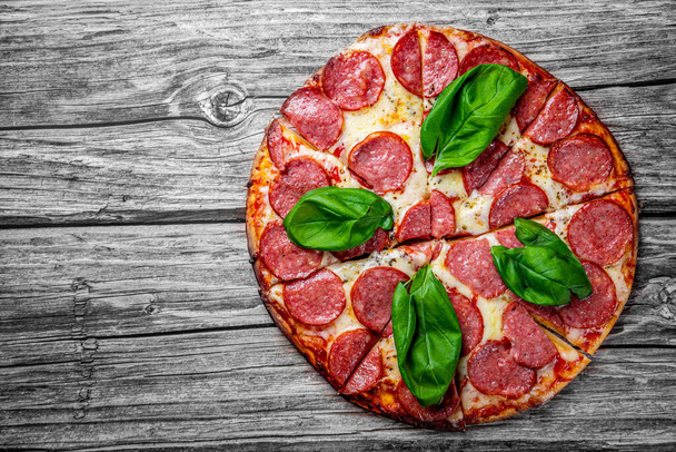 Pepperoni Pizza with Mozzarella cheese, salami, Tomato sauce, pepper, Spices and Fresh basil. Italian pizza on wooden table background - Foto, afbeelding