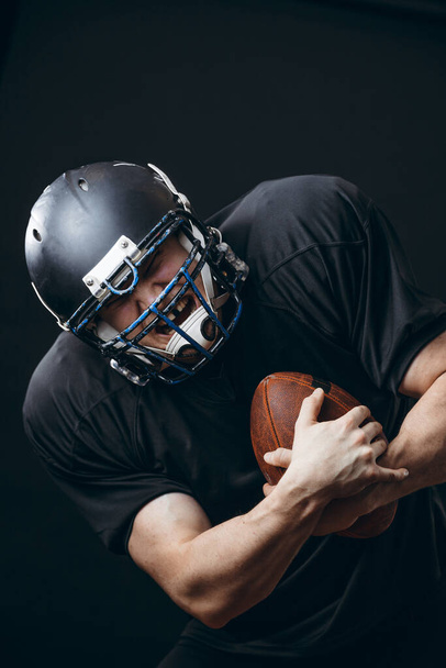 American football sportsman player in action isolated over black studio wall - Foto, afbeelding