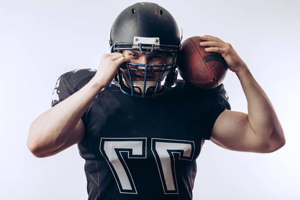 Muscular american football player in protective uniform and helmet holding ball - Foto, immagini