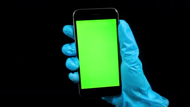 Filmik osoby noszącej rękawiczki trzymającej telefon z zielonym ekranem - Materiał filmowy, wideo