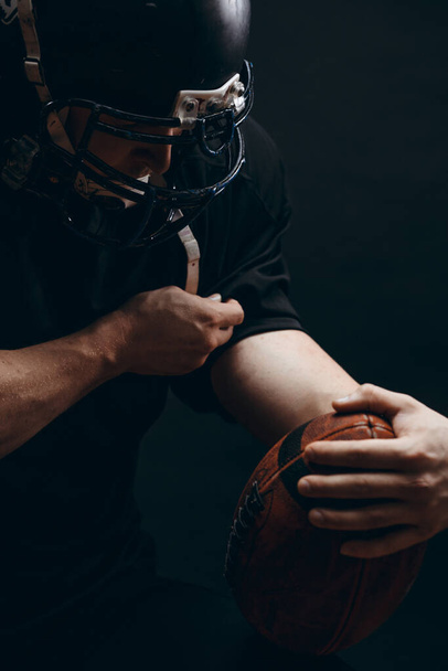 American football player in black sportwear with a ball on black background - Valokuva, kuva