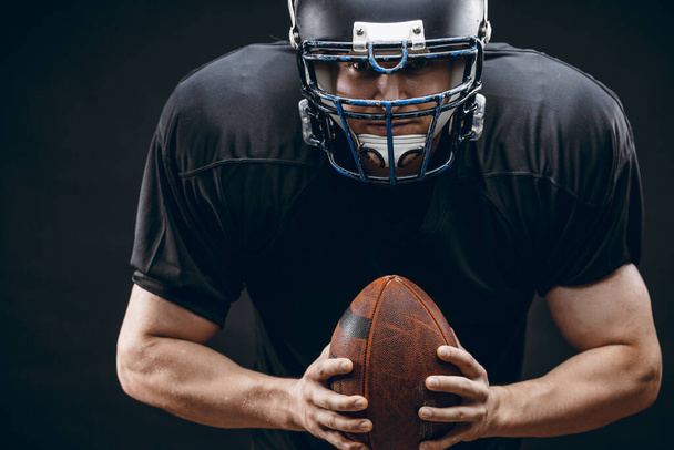American football player in black sportwear with a ball on black background - Foto, Bild