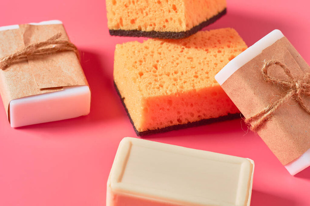 Scattered bricks of soap in vintage packing near sponges on pink background. Hygiene and cleaning concept - Foto, afbeelding