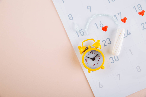 Calendario de menstruación con alarma amarilla y toallas sanitarias diarias sobre fondo rosa. Días críticos para la mujer, concepto de protección de la higiene femenina
 - Foto, Imagen