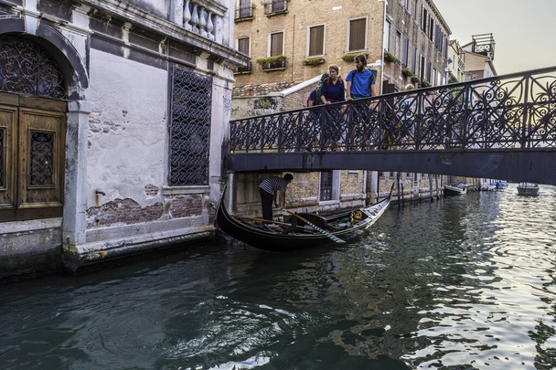 Гондольєр веслує гондолею і готується пройти під дуже низьким мостом у Венеції (Італія). - Фото, зображення