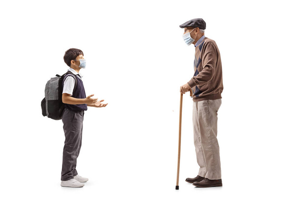 Full length profile shot of a schoolboy talking to his grandfather and wearing a protective face mask isolated on white background - Photo, image
