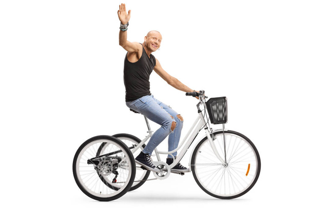 Profile shot of a bald guy riding a tricycle and waving at the camera isolated on white background - Zdjęcie, obraz