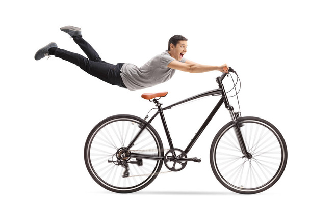 Guy flying and holding onto a bicycle isolated on white background - 写真・画像