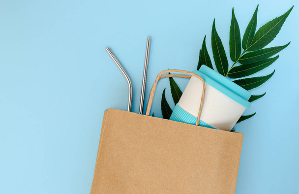 Paper bag with bamboo cup and reusable drinking straws on blue background. Mockup, top view. Zero waste concept - Fotografie, Obrázek