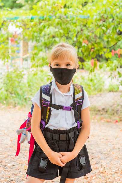 Schoolgirl girl in a black protective mask with a backpack. Schoolgirl in a school uniform. Fall. Back to school soon. - Фото, изображение