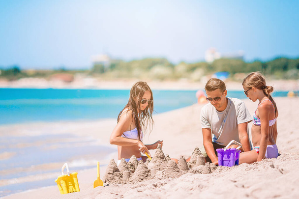 Isä ja lapset tekevät hiekkalinnaa trooppisella rannalla. Perhe leikkii ranta leluja - Valokuva, kuva