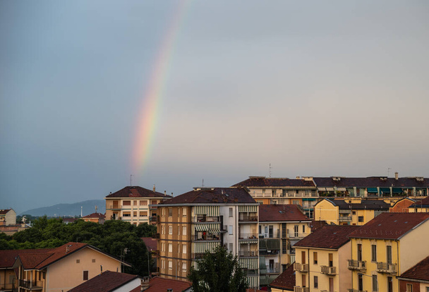 Torino, Piemonte, Italia. Giugno 2020. Dopo una tempesta estiva nella periferia settentrionale, un arcobaleno emerge dal tetto di una piccola casa all'orizzonte e abbraccia la città.. - Foto, immagini