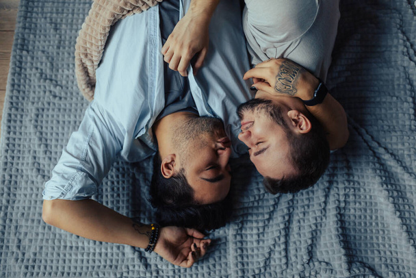 Handsome sleepy man with bristle kissing good night male partner lying in bed - Fotografie, Obrázek