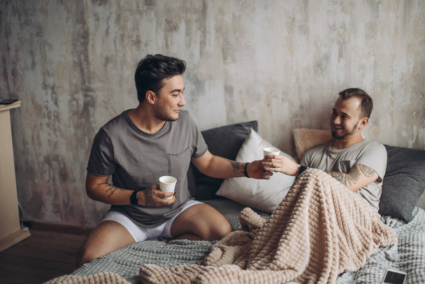 Idealny poranek zaczyna się od kochanka i kawy w łóżku. Dwóch facetów odpoczywających w łóżku.. - Zdjęcie, obraz