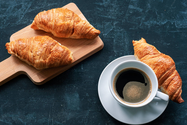 Šálek kávy a croissanty na černém stole, výhled shora. Ranní snídaně koncept - Fotografie, Obrázek