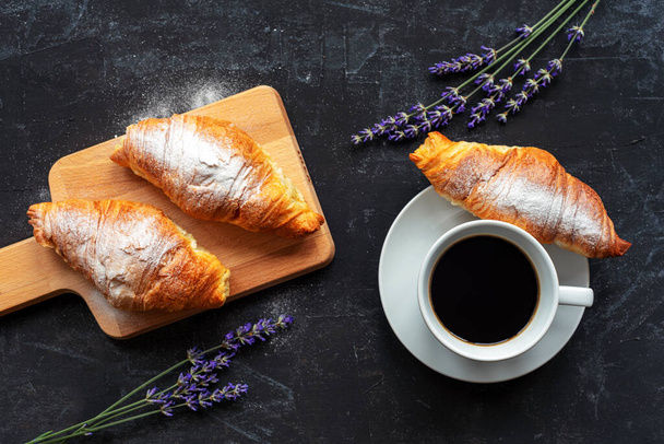 Kuppi kahvia ja croissanteja, laventelin kukkia mustalla pöydällä, ylhäältä. Aamupala käsite - Valokuva, kuva