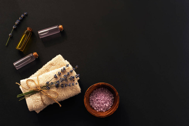 Meersalz, Handtücher mit Lavendelblüte und ätherischen Ölen auf schwarzem Hintergrund, Draufsicht, flache Lage, Kopierraum - Foto, Bild