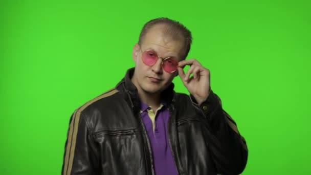 Jóképű rocker férfi rózsaszín napszemüvegben, ujjal mutogat rád, a kamerába néz, választ. - Felvétel, videó