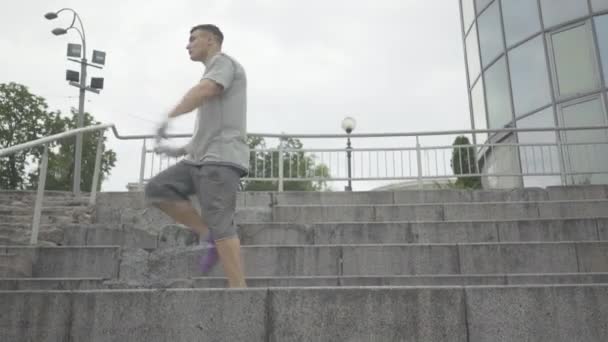 Back flipping of young confident Caucasian man on urban stairs. Wide shot portrait of handsome brunette dancer performing on city street on summer day. - 映像、動画
