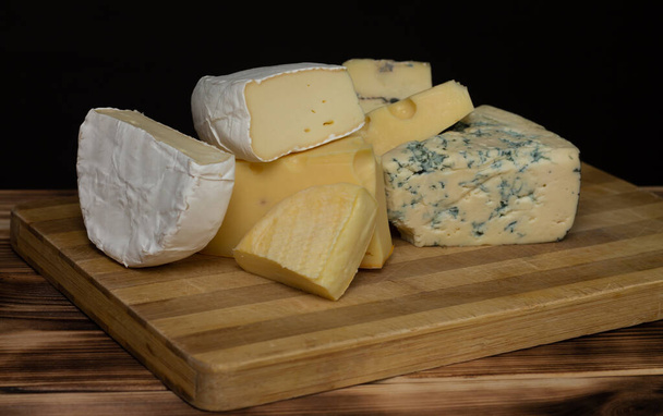 Diferentes tipos de queso en una tabla de cortar de madera rústica sobre un fondo oscuro
 - Foto, imagen