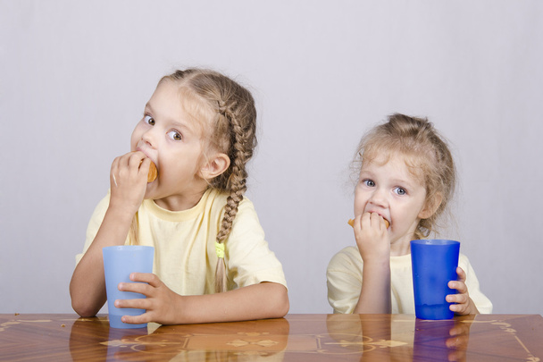 Kaksi lasta syö muffinin pöydässä.
 - Valokuva, kuva
