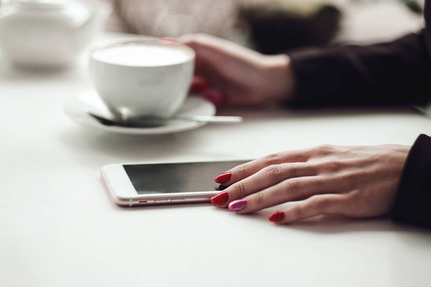 Manos de mujer con teléfono inteligente, auriculares y taza de té. Para montaje gráfico de pantalla - Foto, imagen