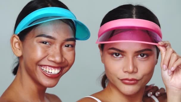 Güneşlik şapkalı iki güzel Asyalı kadının portresi beyaz arka plandan kameraya bakıp gülümsüyor. - Video, Çekim