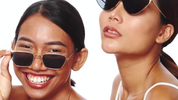 Portret van twee jonge lachende Aziatische vrouwen lachend, poserend in een zonnebril over een witte achtergrond - video in slow motion - Video