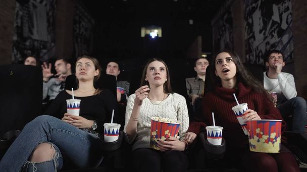 Drei hübsche Freundinnen sehen sich einen gruseligen Film an.Mittlere Frau reagiert schockiert. - Foto, Bild