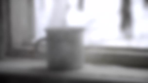 Unscharfer Hintergrund. Eisenkrug alt steht auf Fensterbank neben Fenster und kocht - Filmmaterial, Video