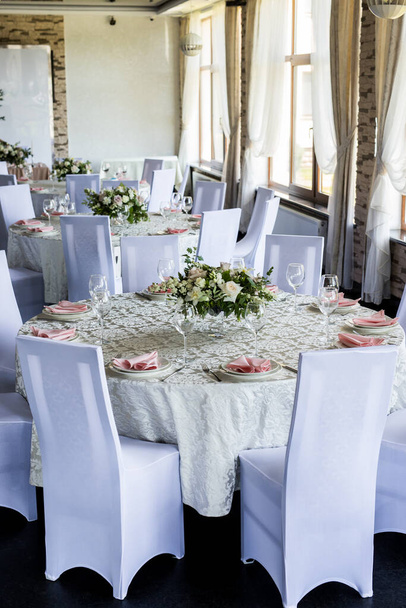 Großaufnahme von zwei festlich gedeckten Tischen mit Weingläsern und frischen Blumen. Selebration Bankett mit rosa Servietten, weißen Tellern und Weingläsern im Restaurant - Foto, Bild