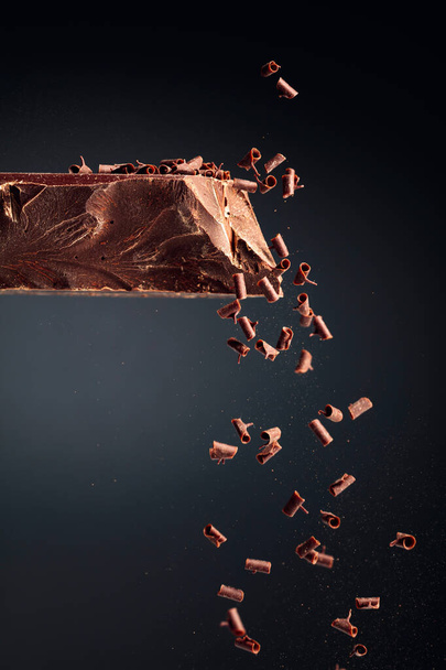Grande pedaço de chocolate escuro e migalhas de chocolate em queda em um fundo preto. - Foto, Imagem