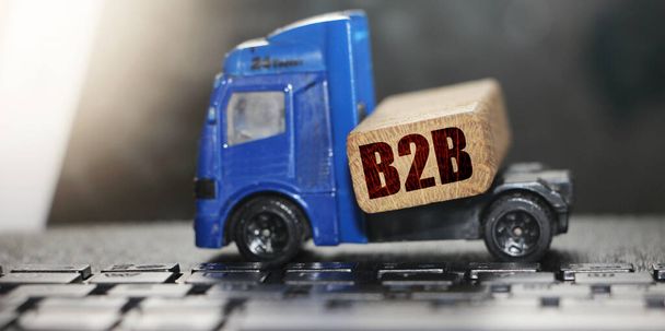 Φορτηγό παιχνιδιών μετακινεί μια παλέτα με ξύλινο μπλοκ με συντομογραφία B2B. Επιχείρηση προς Επιχείρηση. Λογιστική έννοια της διανομής δικτύου και της μεταφοράς φορτίου. - Φωτογραφία, εικόνα