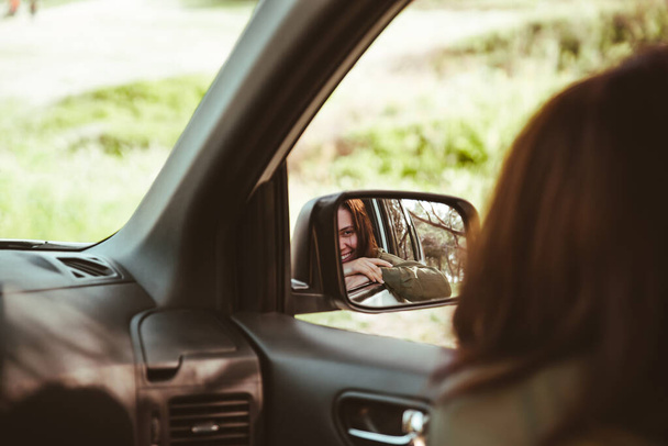 refleksja nad oszałamiającą uśmiechniętą kobietą w tylnym lusterku samochodu. wynajem samochodu koncepcja - Zdjęcie, obraz